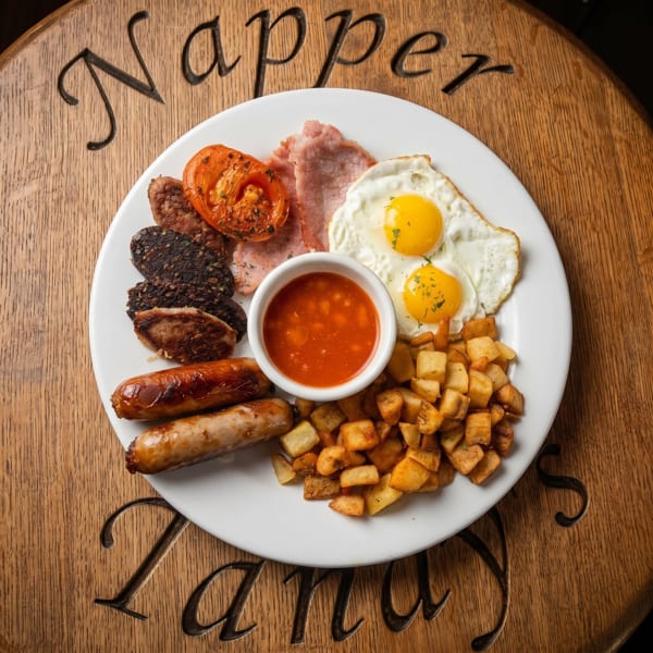 A full Irish breakfast with eggs, bacon, sausages, black pudding, tomatoes, beans, and potatoes.