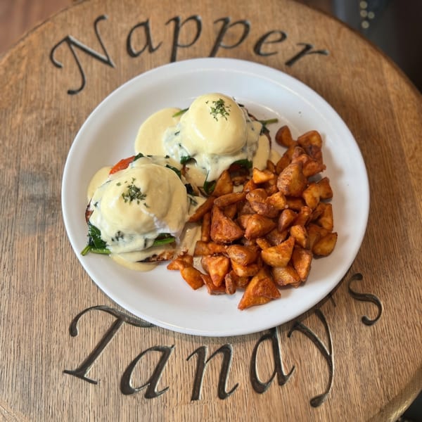 Eggs Benedict with hollandaise sauce and a side of roasted potatoes on a white plate.