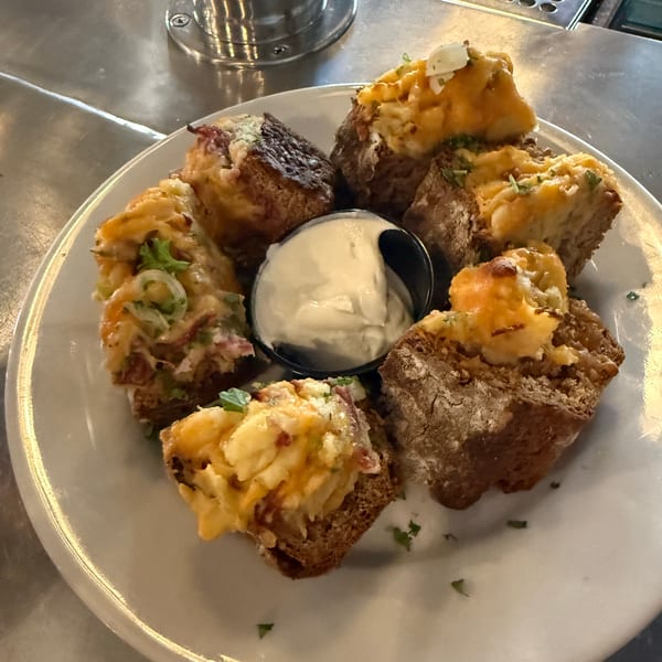 A plate of loaded potato skins on dark bread with a side of sour cream.
